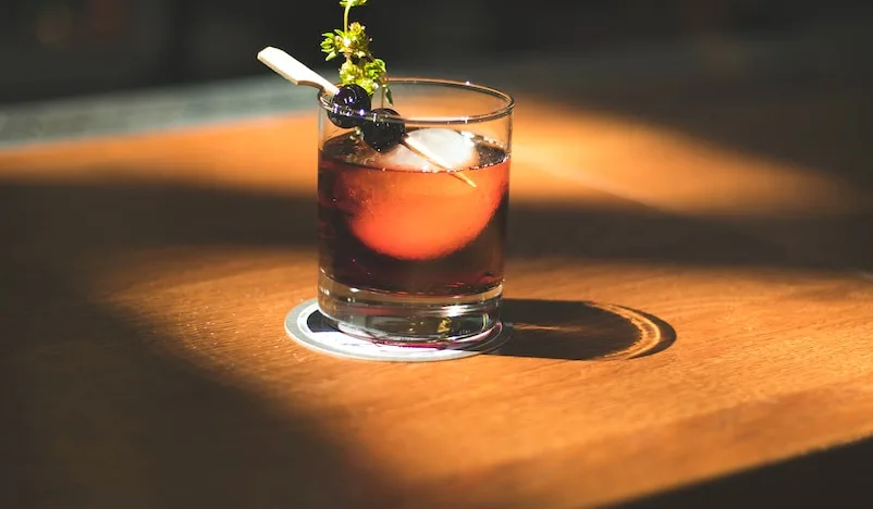 brown beverage with olives and herb in rocks glass in macro photography